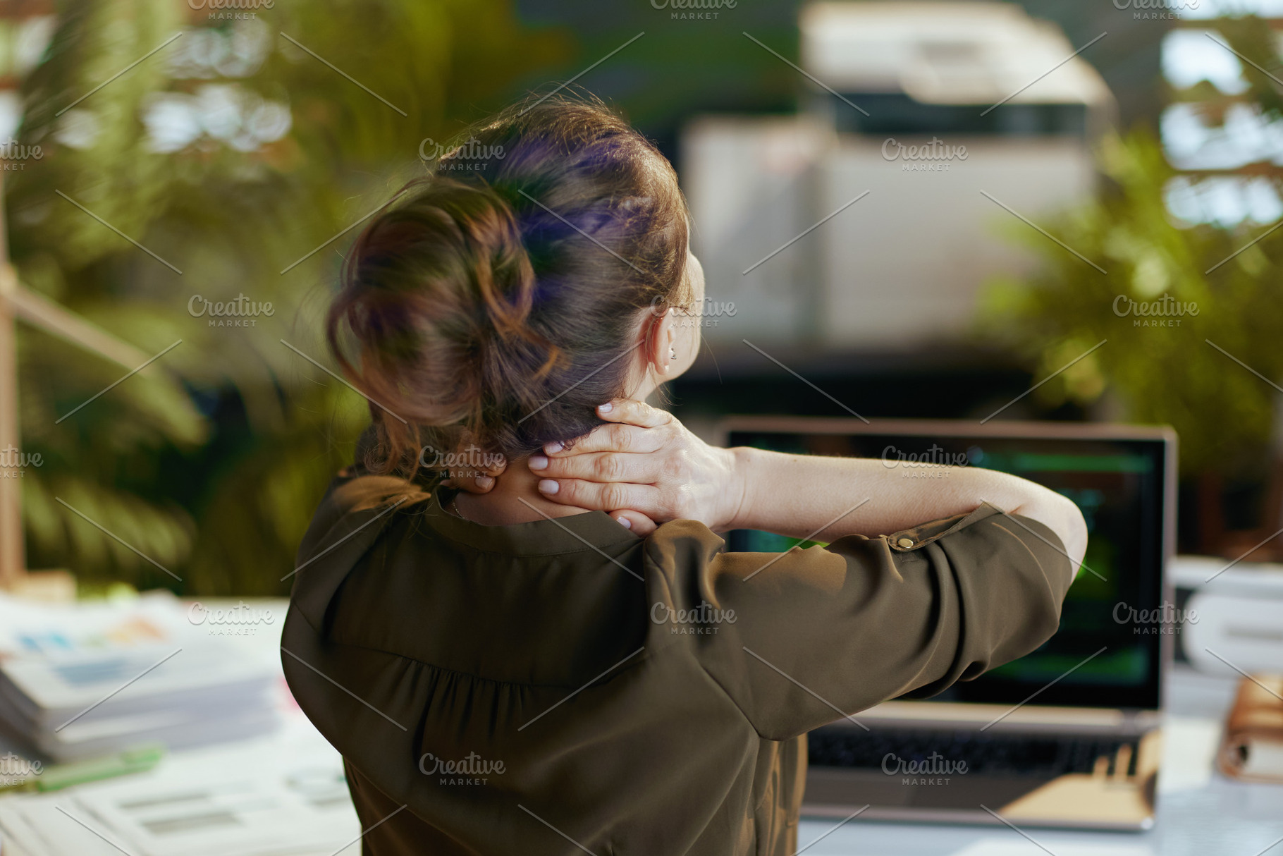 Seen from behind modern woman with laptop having neck pain, a Business Photo by Alliance Images
