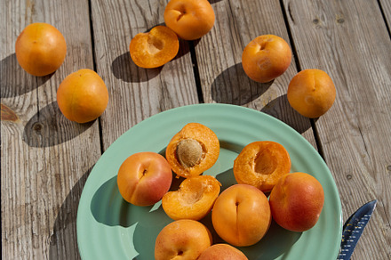 Whole and halved apricots on turquoise plate with knife on rustic wooden table