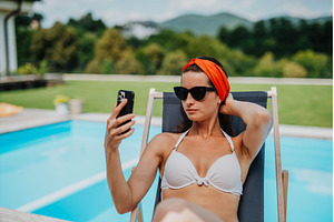 Young woman sitting by swimming pool, a Person Photo by HalfPoint