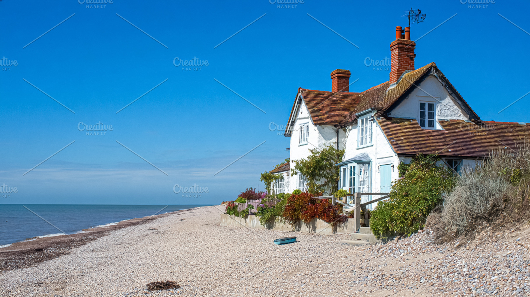 White cottage standing on a pebble beach with a gentle ocean and, a Photo by Studio ANNA