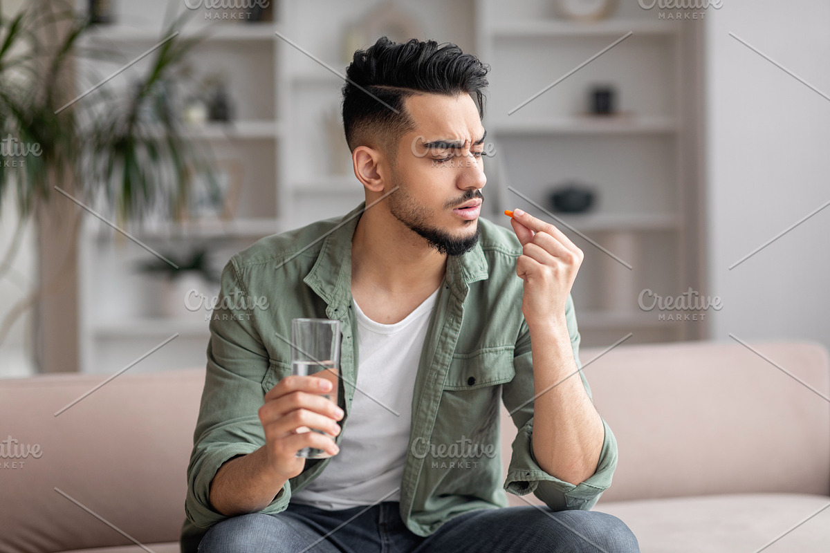 Sad young arab man with beard in casual sits on sofa with glass of water and lo, a Photo by Prostock-Studio (Photo 1 of 2)