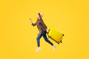 Female Tourist Running In Mid Air Carrying Suitcase, Yellow Background, a Photo by Prostock-Studio