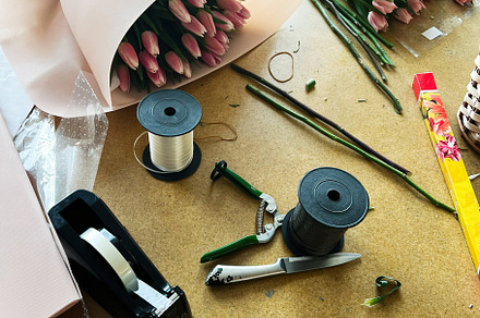 Florist arranging pink tulips bouquet with tools on a wooden workspace, a Photo by AS photostudio