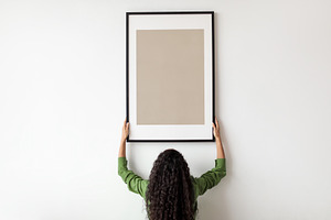 Unrecognizable Female Hanging Blank Poster In Frame On Wall Indoor, a Photo by Prostock-Studio