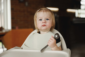 Infant girl or toddler sitting on high chair. Eating food by herself using spoo, a Person Photo by Lenor4ik