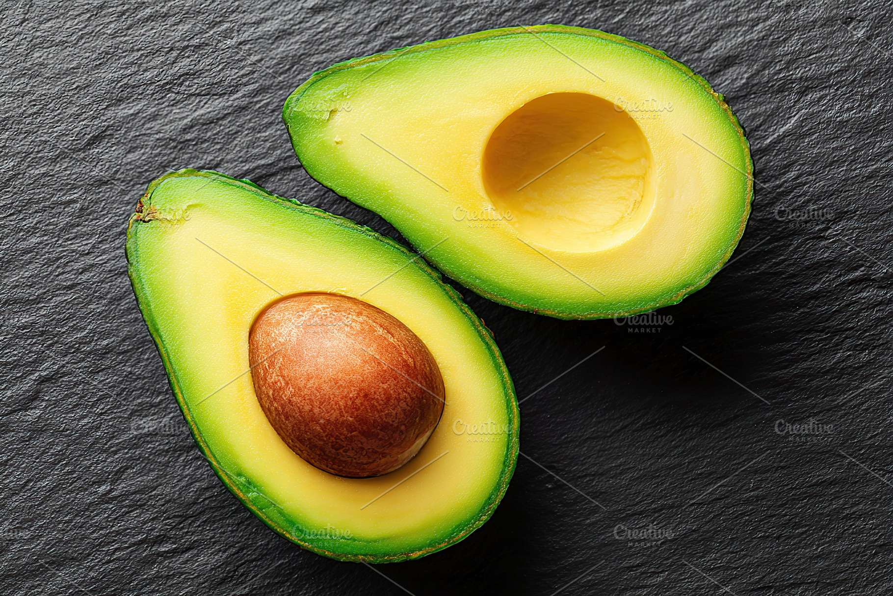 Halved avocado on dark slate background showcasing its creamy texture and healt, a Food & Drink Photo by AlyaAnd