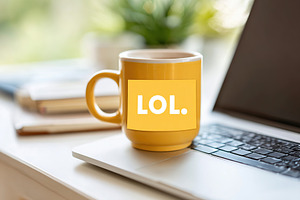 Laptop with broken M key and yellow mug displaying LOL sticker on a desk, a Photo by AlyaAnd