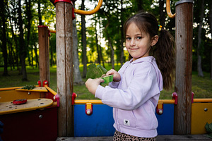 Smiling girl holding green leaves at a colorful playground in a forested park, a Person Photo by AS photostudio