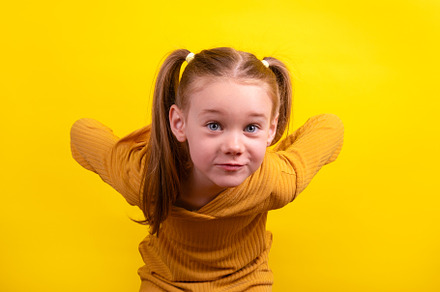 Cheerful young girl with pigtails and mustard yellow sweater pla
