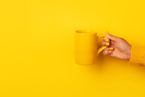 Hand in yellow sweater holding a plain yellow ceramic mug horizo, a Food & Drink Photo by Ales Munt