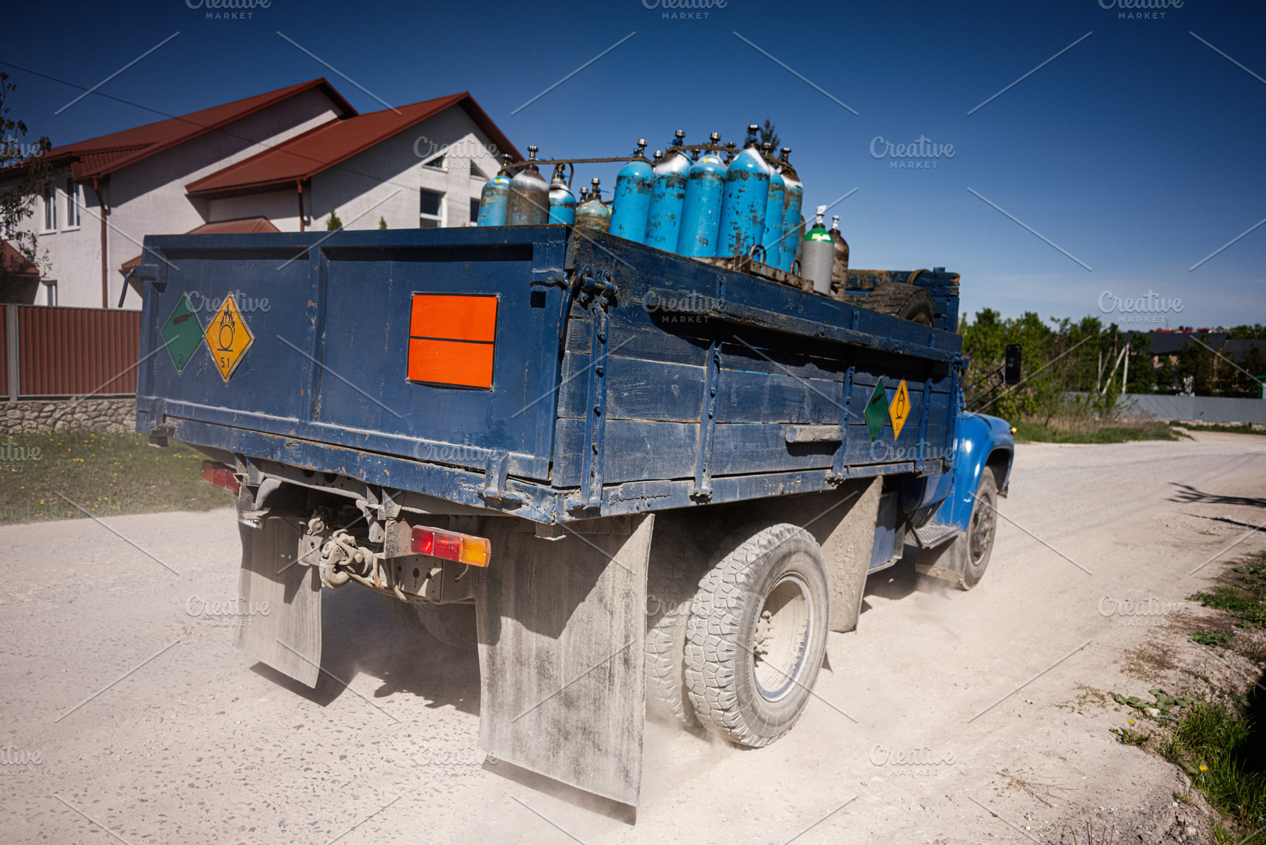 Blue cargo truck carrying gas cylinders on rural road under clear sky, a Photo by AS photostudio