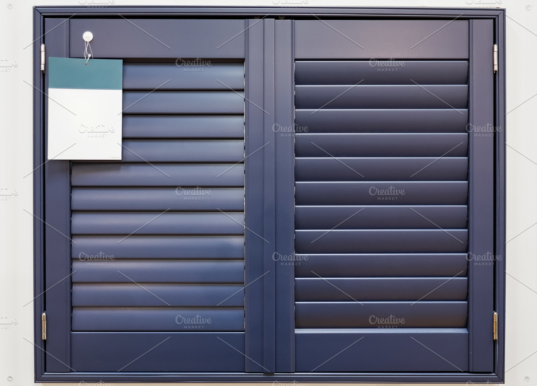 Dark blue folding plantation shutters covering a window with a blank sample tag, a Photo by Studio ANNA