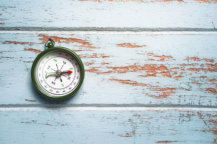 Green compass on wooden board featuring adventure, arrow, and atlas