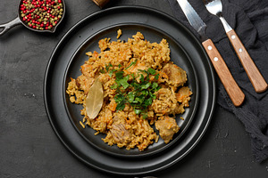 Pilaf with rice and pieces of meat in a black round plate on the, a Food & Drink Photo by ndanko