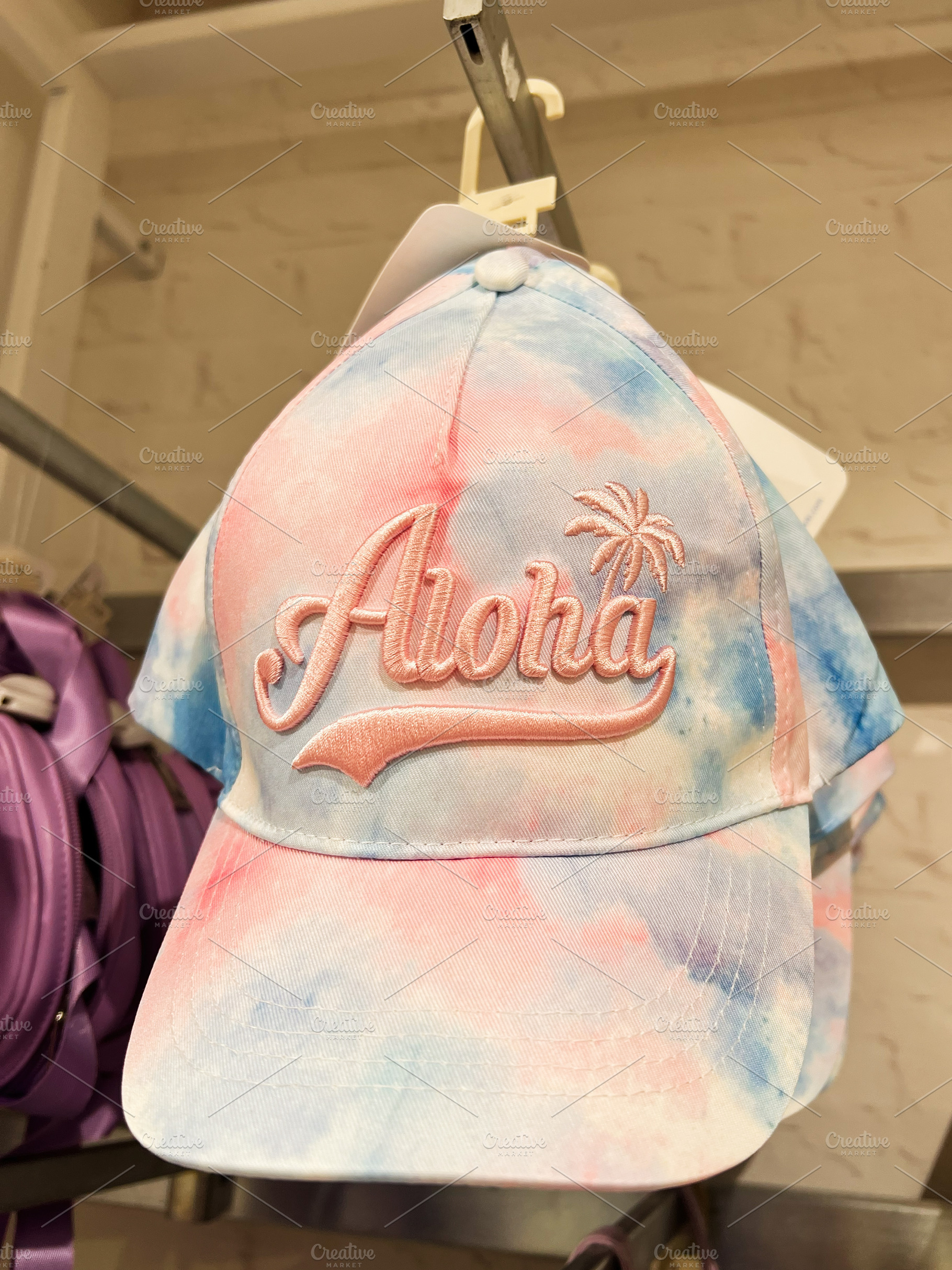 Colorful tie dye cap with 'Aloha' text displayed in a retail store, a Photo by AS photostudio