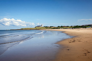 Wide sandy beach with gentle waves on a sunny day. Coastal town, a Photo by Studio ANNA