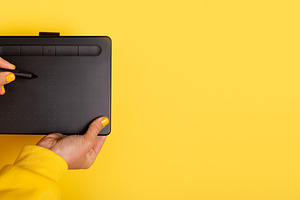 Person holding a digital drawing tablet and stylus against a bri, a Technology Photo by Ales Munt