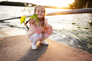 Young girl enjoying sunset by a lake holding flowers with a joyful smile, a Photo by AS photostudio