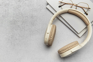 Modern wireless headphones lying on table next to books and eyeg, a Business Photo by Olena Rudo
