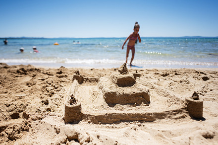 Child playing near a detailed sandcastle on a sunny beach day, a Person Photo by AS photostudio