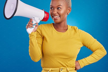 Black woman, megaphone and smile, protest and voice, freedom of speech and activism on blue background. Happy female, broadcast and speak out, rally and activist, loudspeaker with opinion in studio, a Photo by Peopleimages.com
