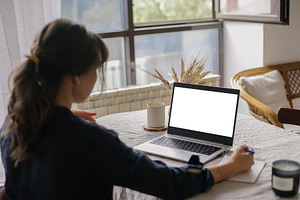 White screen on laptop. Mockup. Young woman working remotely on laptop computer