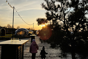 Two people walking on a sunset-lit wooden path near outdoor structures, a Photo by AS photostudio