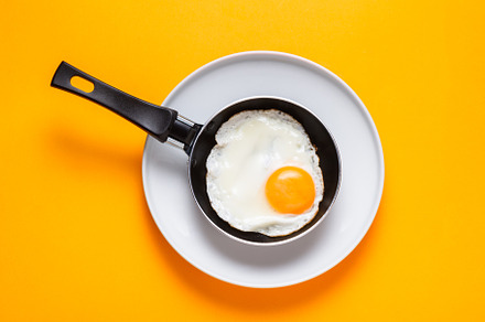 Scrambled, frying  eggs from one egg in a small pan on yellow ba, a Food & Drink Photo by MDBildes