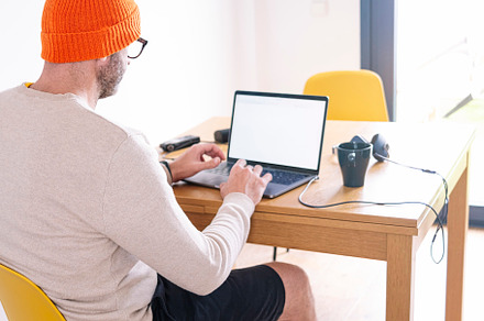 Unrecognizable man working from home on a laptop sitting at a desk surfing the, a Person Photo by karrastock