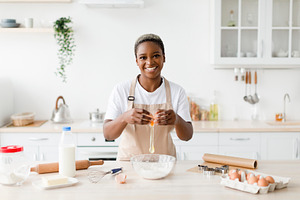 Cheerful young pretty black female in apron breaks egg, prepare baking pie or p, a Person Photo by Prostock-Studio