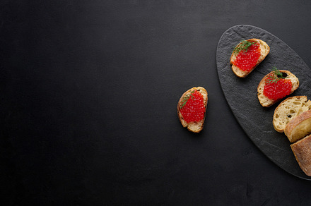 Red caviar on slices of white wheat bread on a black table, conc, a Food & Drink Photo by ndanko