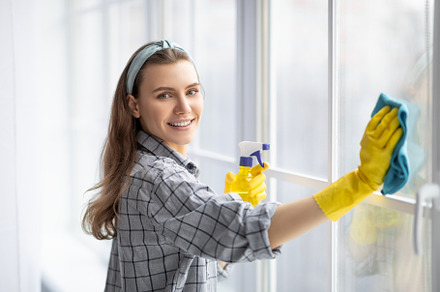 Smiling young woman with detergent and rag cleaning window glass. Professional, a Photo by Prostock-Studio