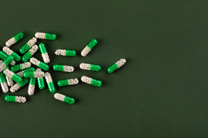 White and green medicine capsules spill from a bottle onto a textured green sur, a Health & Medical Photo by Ales Munt