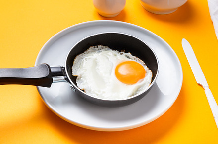 Scrambled, frying  eggs from one egg in a small pan on yellow ba, a Food & Drink Photo by MDBildes