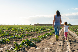 Woman farmer and little girl walking featuring woman, child, and garden