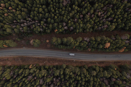Road with cars between deep green forest in Ural