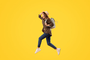 Happy Tourist Lady With Backpack Jumping Over Yellow Background, a Photo by Prostock-Studio