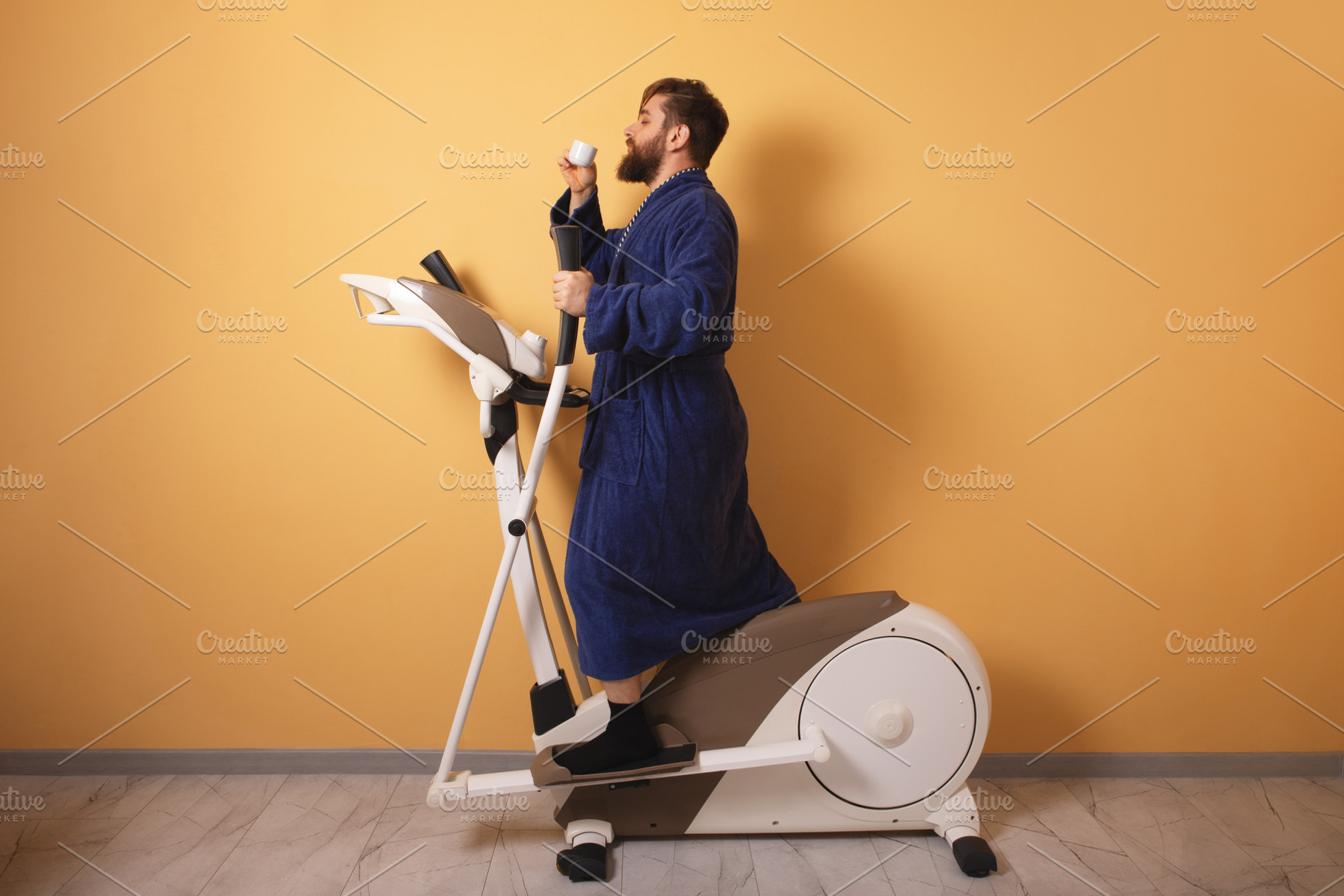 Bearded man in blue bathrobe drinks coffee while exercising on e, a Person Photo by Ales Munt