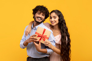 Portrait of loving indian couple holding wrapped gift for Valentine's Day toget, a Person Photo by Prostock-Studio