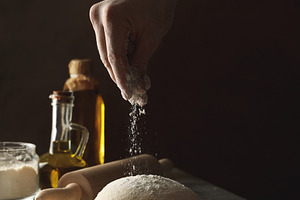 Man sprinkle flour on dough against dark background, a Food & Drink Photo by AtlasStudio PRO