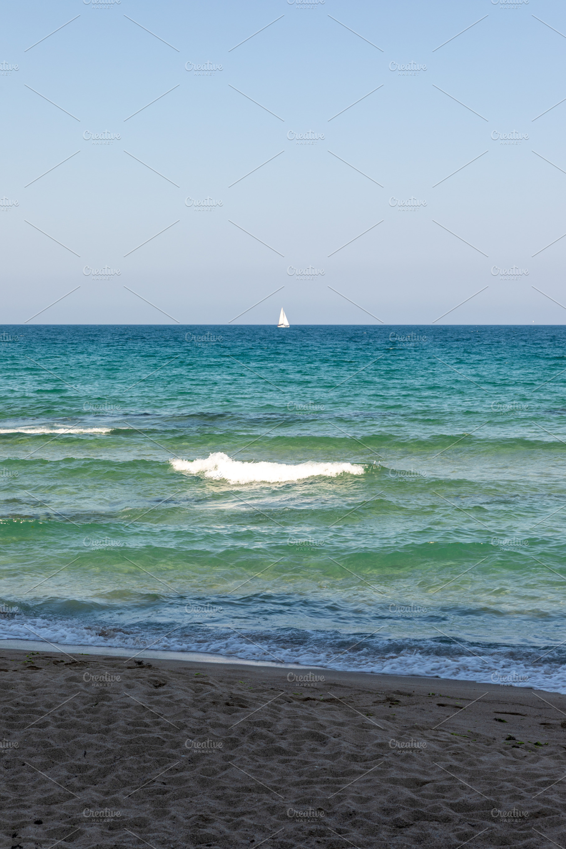Calm turquoise waves roll onto a sandy beach under a clear blue sky, with a dis, a Nature Photo by Ales Munt