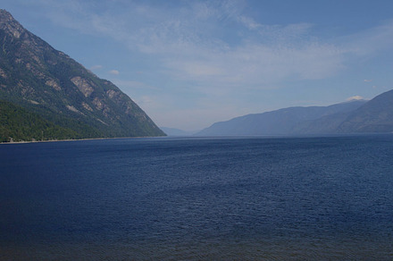 Lake Teletskoye between mountains with blue clear sky in Altai, a Nature Photo by TravelFlow