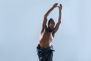 Black shirtless gay model with hands raised posing in blue studio, a Person Photo by andreonegin market