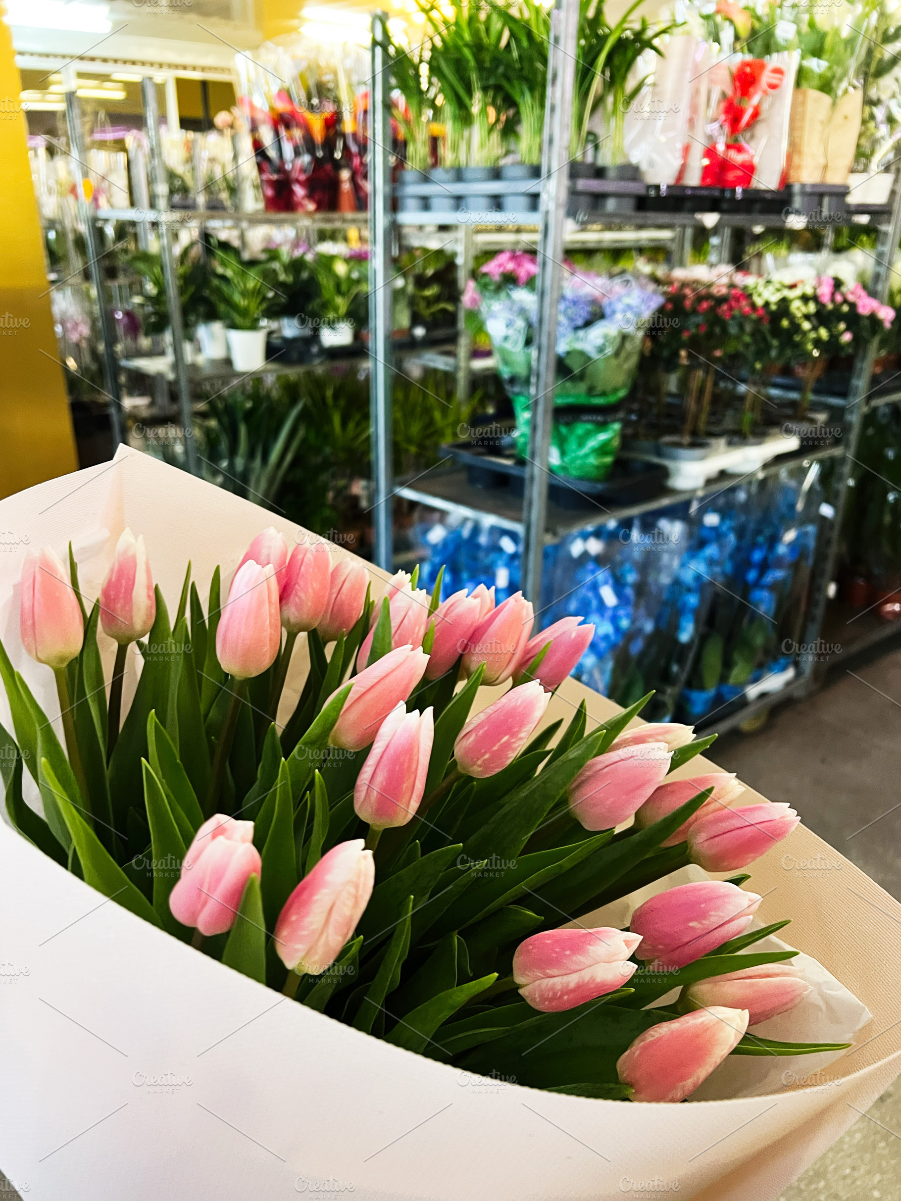 Bouquet of pink tulips arranged in a flower shop with various plants visible, a Photo by AS photostudio