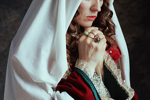 medieval queen in red dress with veil and crown praying, a Person Photo by Alliance Images