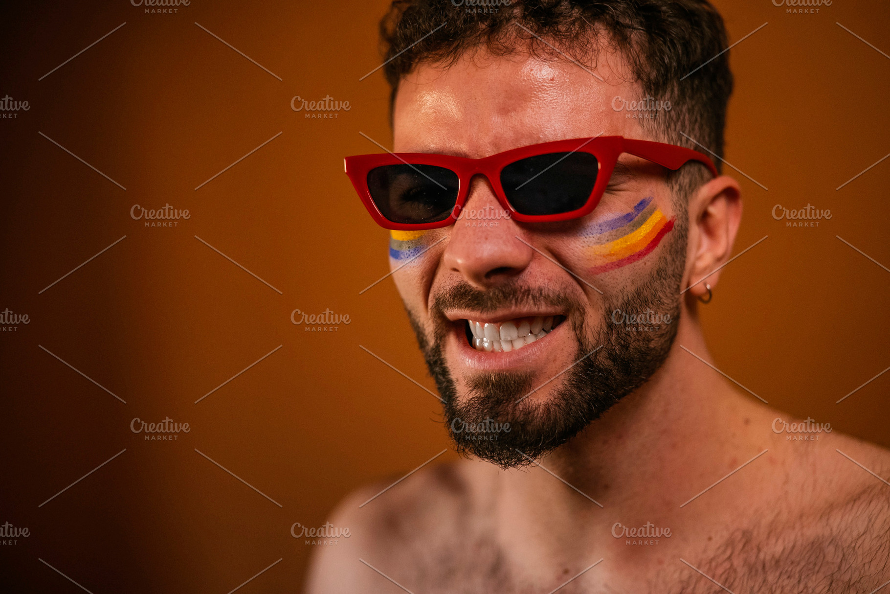 Man in red sunglasses with rainbow face paint celebrating, a Photo by karrastock