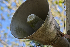 An old, dirty, grey loudspeaker is mounted on a pole. In the bac, an Abstract Photo by ndanko