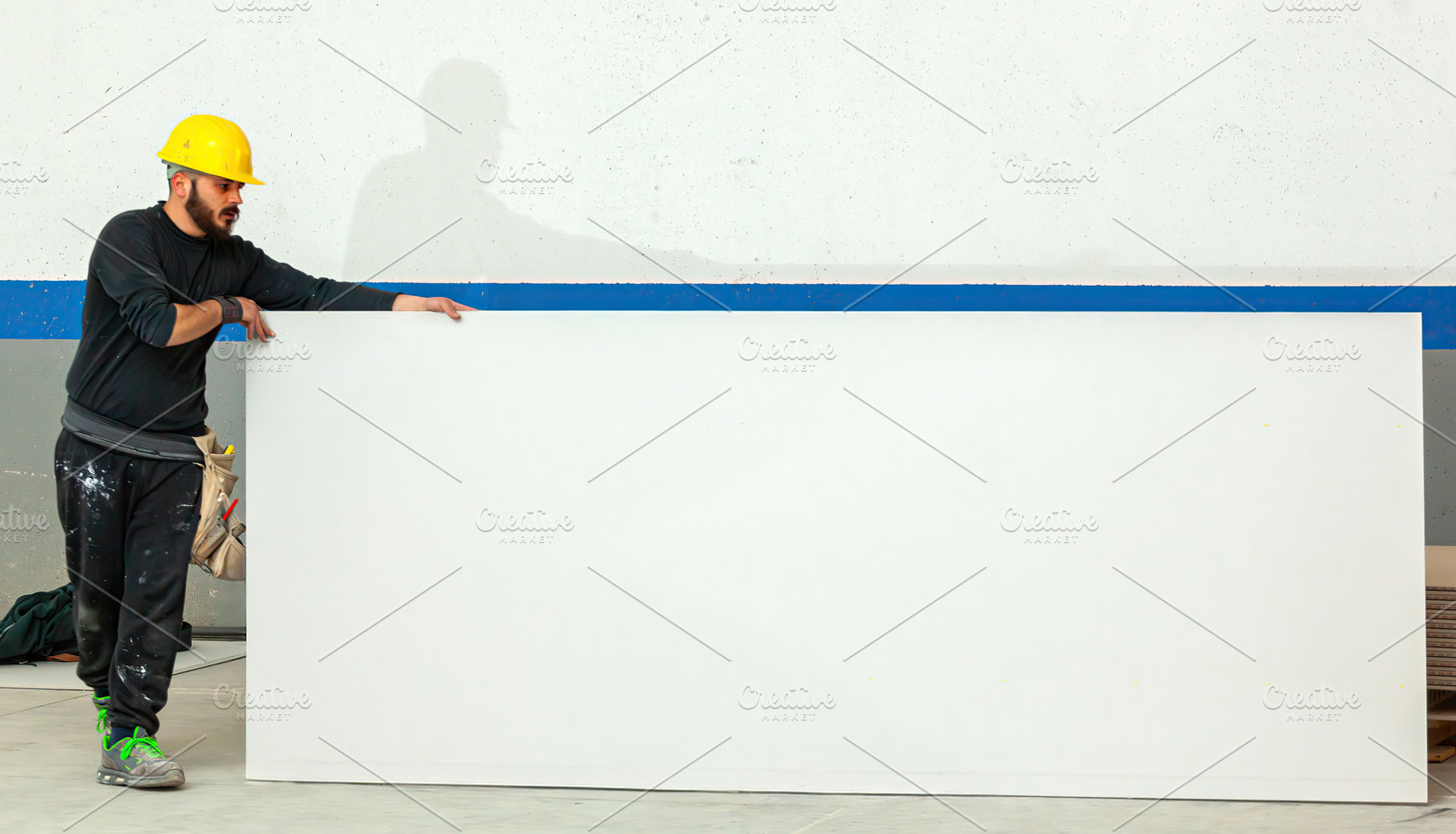 Construction worker holding large white plasterboard sheet in a construction si, an Industrial Photo by Antonio Gravante Market
