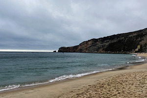 Serene beach with cliffs and cloudy sky in Nazare, Portugal, a Photo by AS photostudio