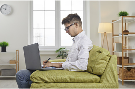 Man sitting on sofa with his laptop, a Technology Photo by StudioRomantic